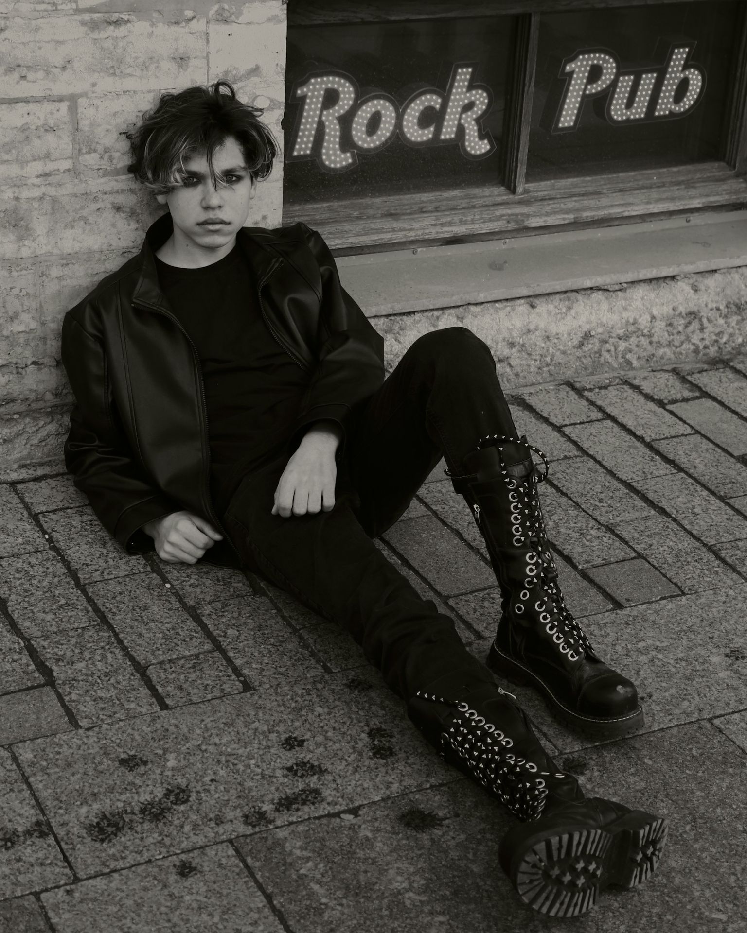 woman in black coat and black pants sitting on concrete pavement
